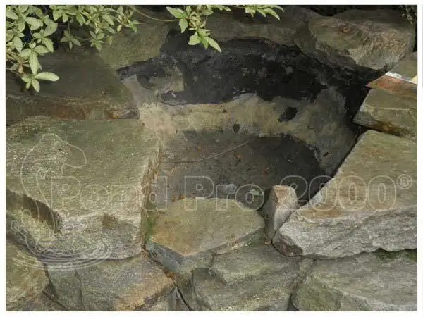 Concrete pond crack and leak area before repair surrounded by stone edging by pondpro2000.com